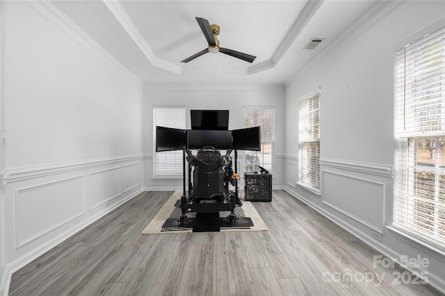 exercise area with crown molding, light hardwood / wood-style flooring, a raised ceiling, and ceiling fan