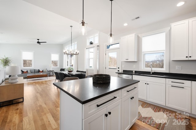 kitchen with hanging light fixtures, light hardwood / wood-style flooring, white cabinetry, dishwasher, and sink