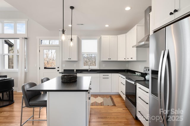 kitchen featuring white cabinets, pendant lighting, stainless steel appliances, wall chimney range hood, and a kitchen bar