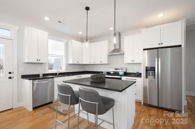 kitchen featuring a center island, white cabinetry, decorative light fixtures, wall chimney range hood, and appliances with stainless steel finishes