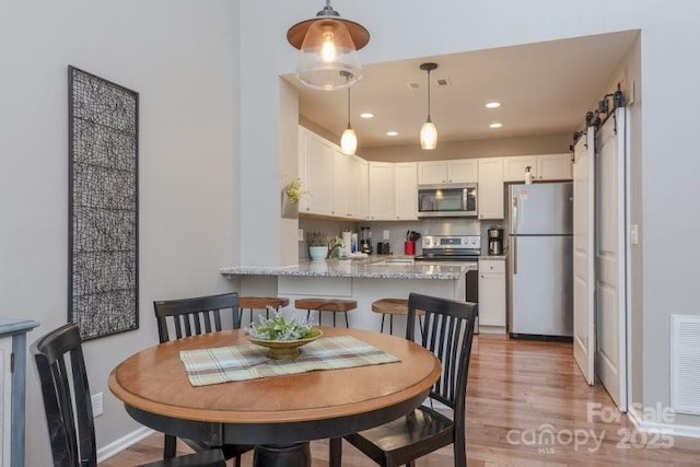 dining area with white cabinetry, hanging light fixtures, light hardwood / wood-style flooring, kitchen peninsula, and a barn door