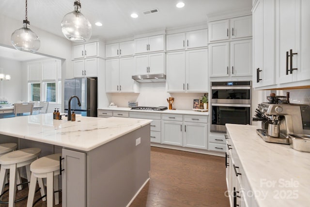 kitchen featuring light stone counters, stainless steel appliances, a kitchen island with sink, and white cabinets