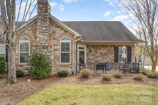 view of front of home with stone siding, a front lawn, roof with shingles, and a chimney