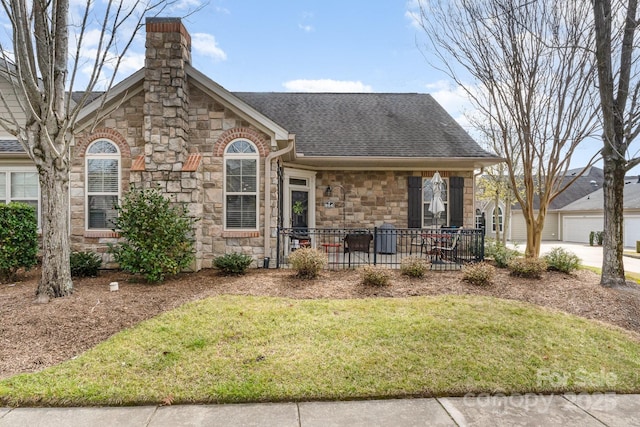 view of front of property with stone siding, roof with shingles, a chimney, and a front yard