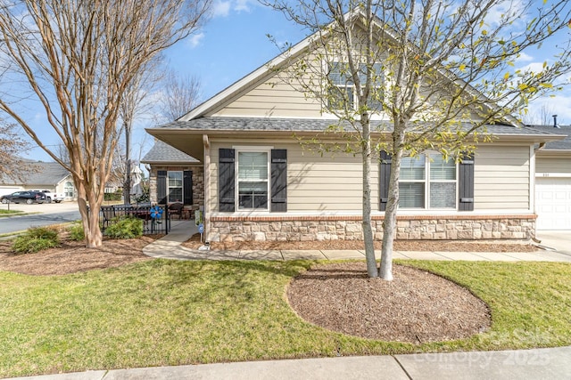 view of front of property featuring a front yard, stone siding, and roof with shingles