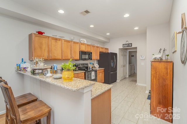 kitchen featuring visible vents, a kitchen breakfast bar, a peninsula, light stone countertops, and black appliances