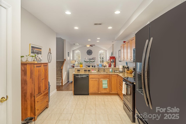 kitchen featuring brown cabinetry, lofted ceiling, a peninsula, black appliances, and a sink