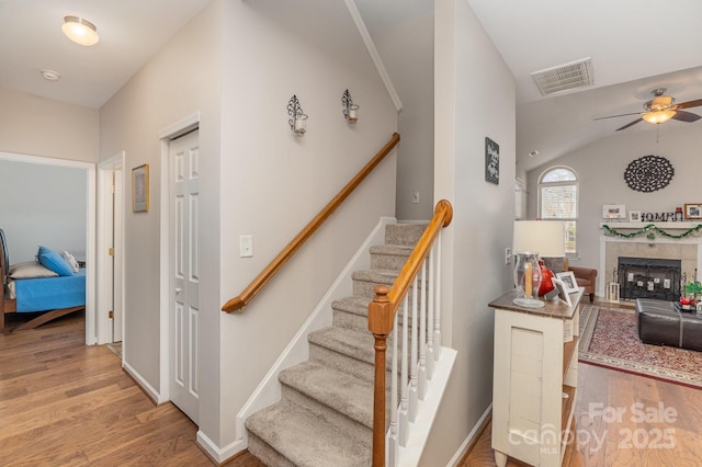 stairs with ceiling fan, wood finished floors, visible vents, vaulted ceiling, and a tiled fireplace