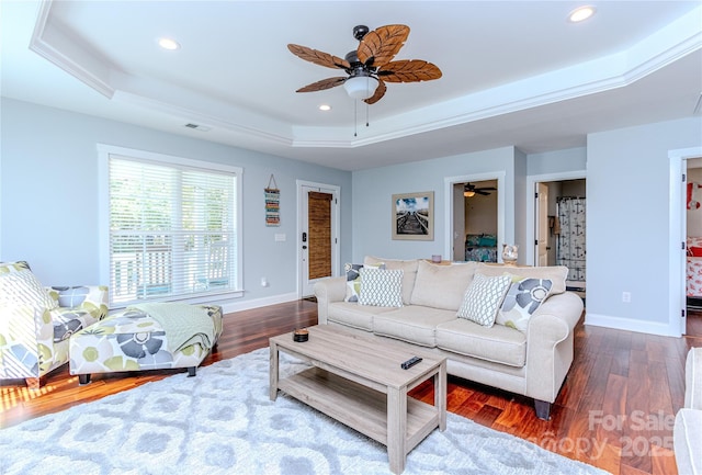 living room featuring dark hardwood / wood-style flooring, a tray ceiling, and ceiling fan