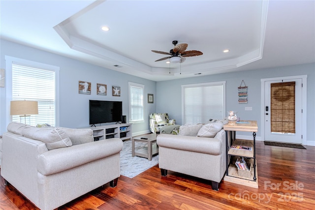 living room with dark wood-type flooring, ceiling fan, and a raised ceiling