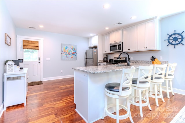 kitchen with sink, a breakfast bar area, white cabinetry, stainless steel appliances, and light hardwood / wood-style floors