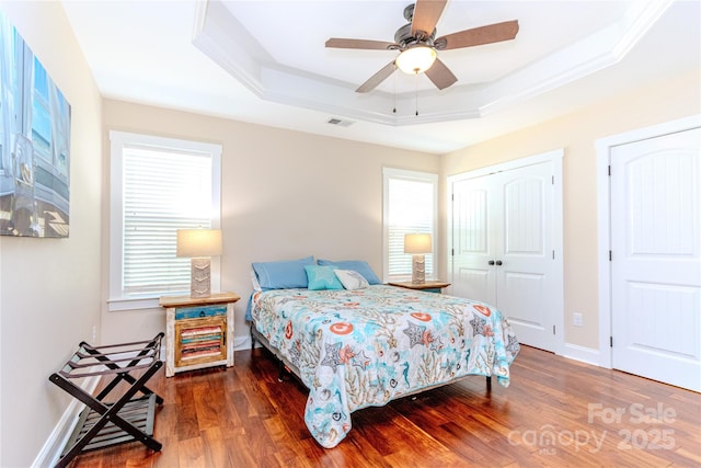 bedroom featuring dark hardwood / wood-style floors, ornamental molding, ceiling fan, a tray ceiling, and a closet