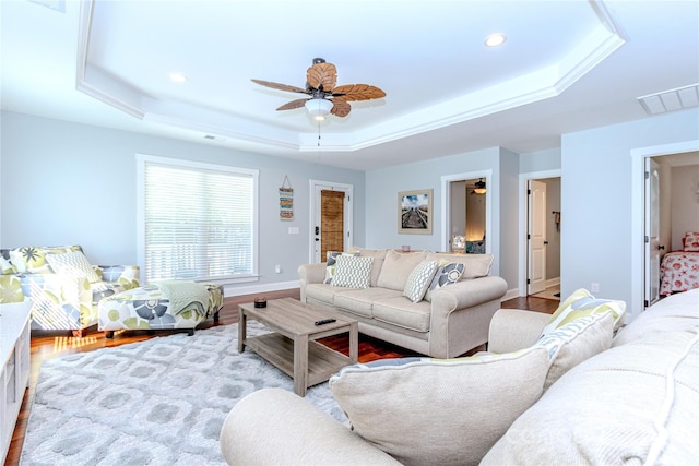 living room with light hardwood / wood-style flooring, a raised ceiling, and ceiling fan