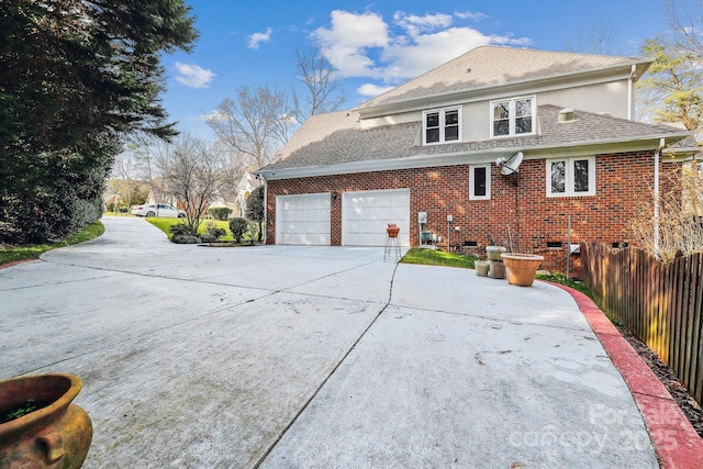 view of side of property featuring a garage, concrete driveway, roof with shingles, fence, and brick siding