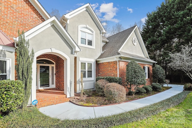 traditional-style home featuring brick siding, a shingled roof, and stucco siding