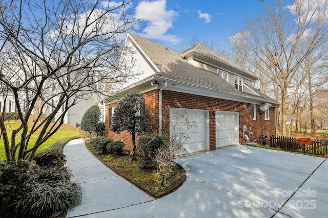 view of side of property with a garage, brick siding, a shingled roof, fence, and driveway