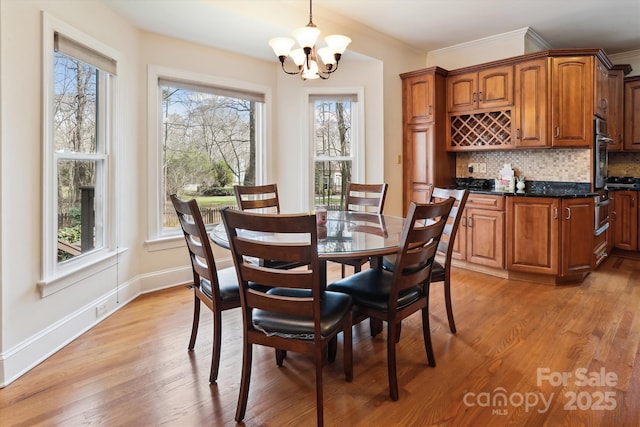 dining space featuring light wood finished floors, baseboards, crown molding, and an inviting chandelier