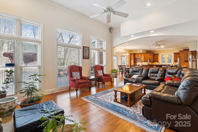 living area featuring arched walkways, light wood-style flooring, a high ceiling, ornamental molding, and ceiling fan