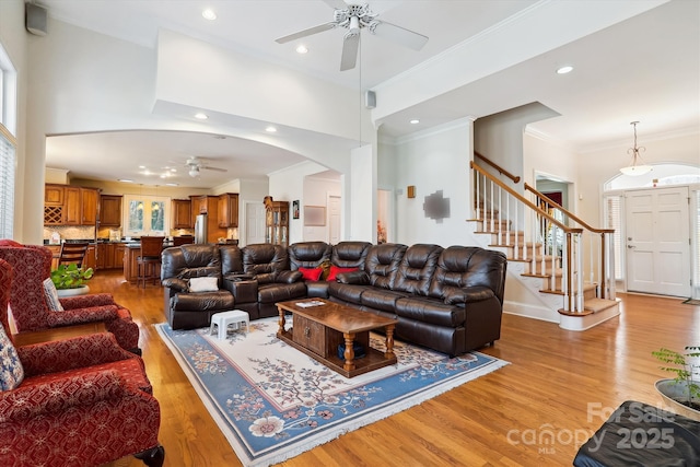 living room with stairway, a towering ceiling, light wood-style flooring, and a ceiling fan