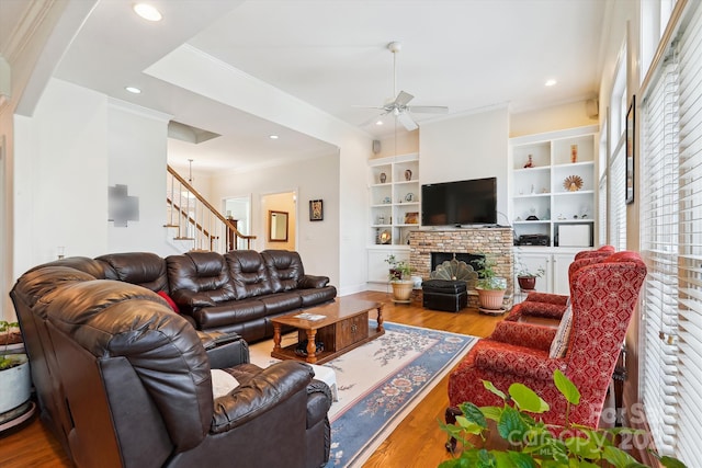 living area with built in shelves, a fireplace, wood finished floors, stairway, and crown molding