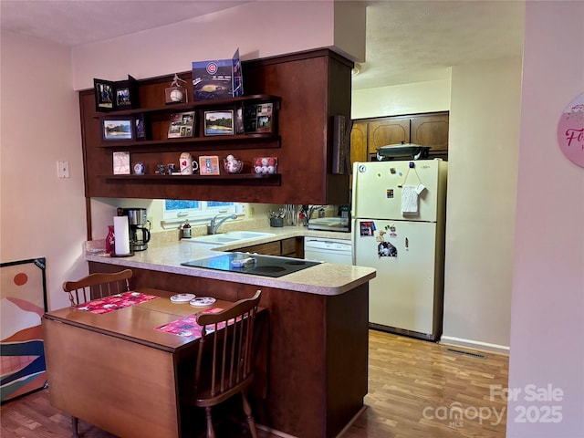 kitchen with sink, black electric stovetop, light hardwood / wood-style floors, kitchen peninsula, and white fridge