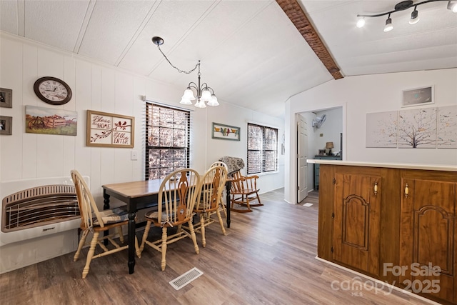 dining room featuring hardwood / wood-style flooring, a notable chandelier, heating unit, and vaulted ceiling with beams