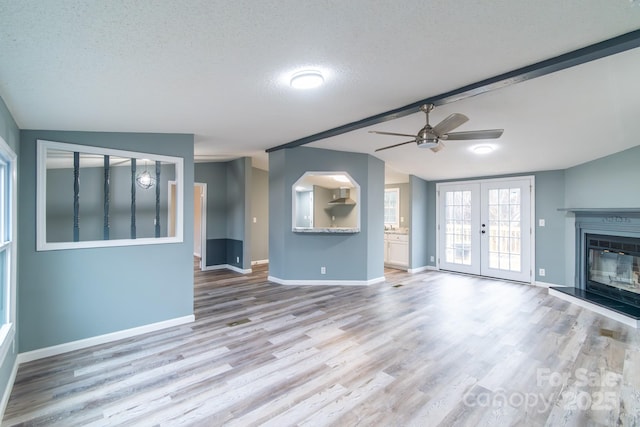 unfurnished living room featuring ceiling fan, vaulted ceiling with beams, light hardwood / wood-style floors, a textured ceiling, and french doors