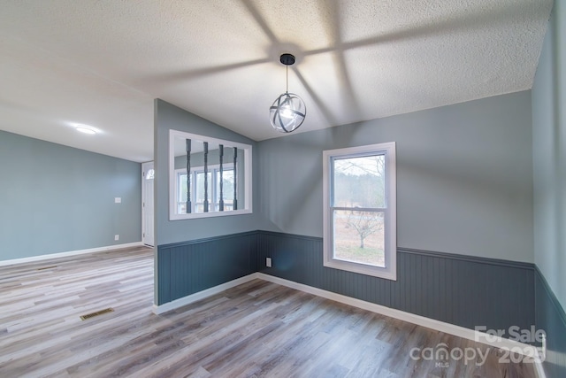 spare room featuring hardwood / wood-style flooring, lofted ceiling, and a textured ceiling