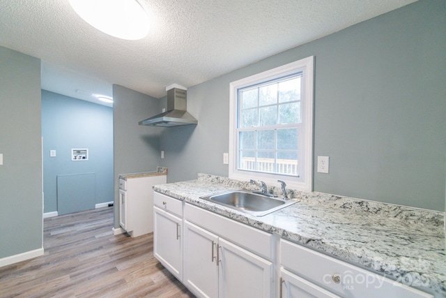 kitchen featuring sink, a textured ceiling, white cabinets, wall chimney exhaust hood, and light wood-type flooring