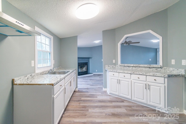 kitchen with extractor fan, white cabinetry, sink, light wood-type flooring, and a textured ceiling