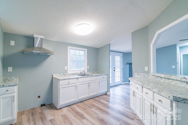 kitchen featuring sink, light hardwood / wood-style flooring, white cabinets, wall chimney range hood, and french doors