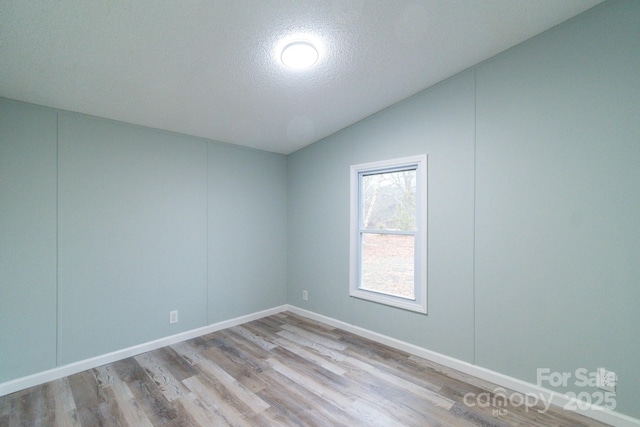 spare room with lofted ceiling, a textured ceiling, and light wood-type flooring