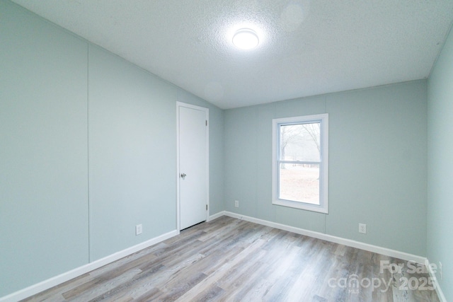 spare room featuring vaulted ceiling, a textured ceiling, and light hardwood / wood-style floors