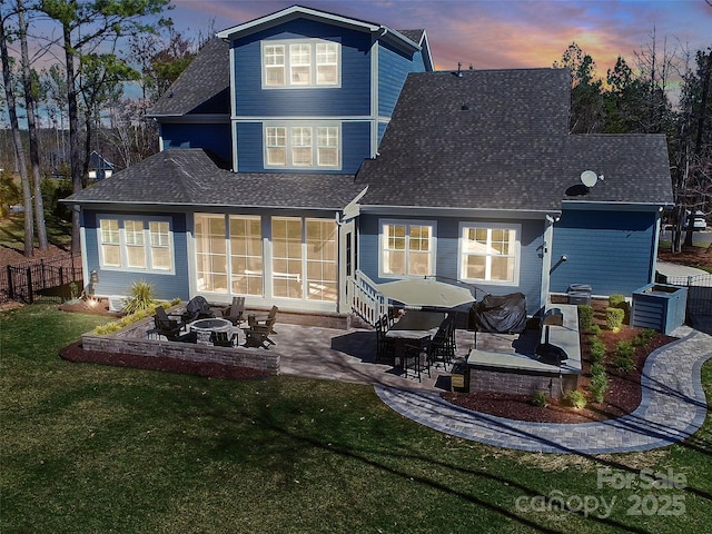 rear view of property with a shingled roof, a patio area, a yard, and a fire pit