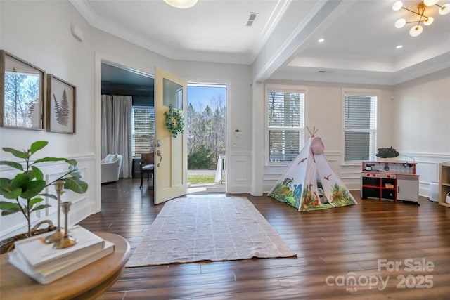 rec room featuring wood-type flooring, a decorative wall, visible vents, and ornamental molding