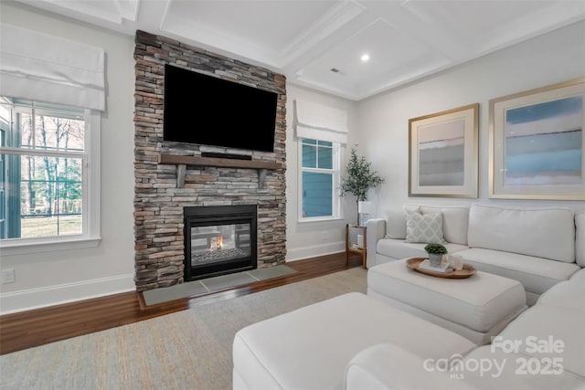 living area featuring coffered ceiling, wood finished floors, a stone fireplace, beamed ceiling, and baseboards