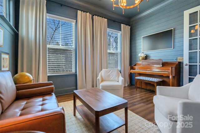 sitting room with wood finished floors, wood walls, ornamental molding, and an inviting chandelier