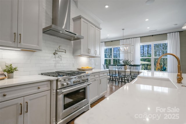 kitchen featuring light countertops, a sink, stainless steel stove, and wall chimney range hood