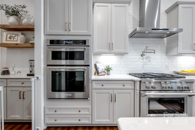 kitchen featuring wall chimney range hood, tasteful backsplash, open shelves, stainless steel appliances, and light countertops