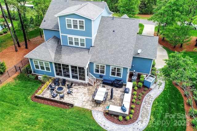back of house with roof with shingles, a fenced backyard, a lawn, a sunroom, and a patio