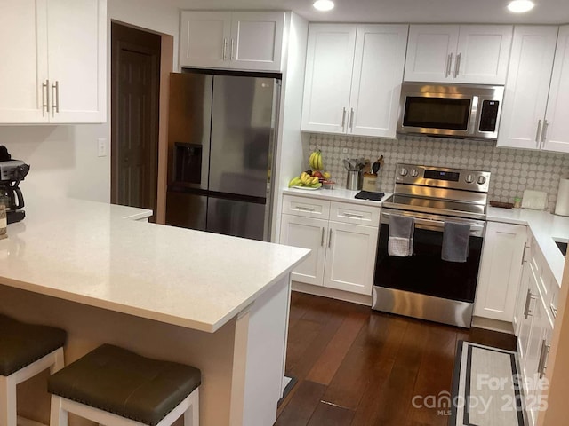 kitchen with appliances with stainless steel finishes, a breakfast bar area, white cabinets, dark hardwood / wood-style flooring, and kitchen peninsula