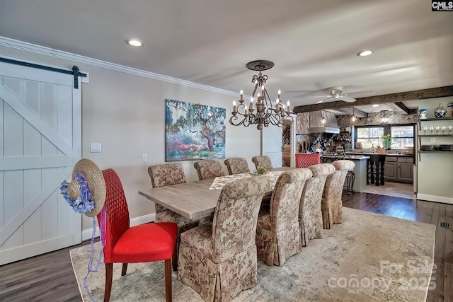 dining area featuring a barn door, baseboards, a ceiling fan, ornamental molding, and wood finished floors