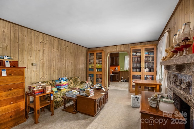 living room with wooden walls, a stone fireplace, and light colored carpet