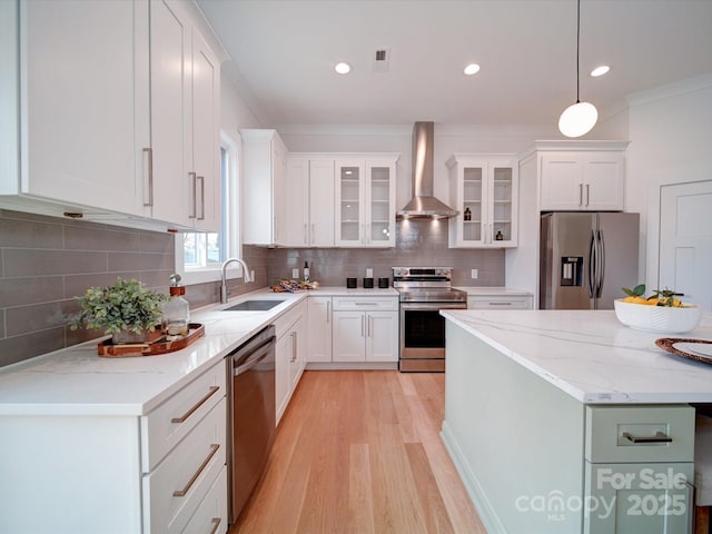 kitchen with wall chimney range hood, sink, white cabinetry, hanging light fixtures, and stainless steel appliances