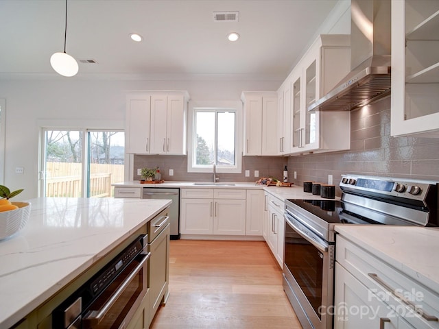 kitchen with white cabinetry, appliances with stainless steel finishes, wall chimney range hood, and decorative light fixtures