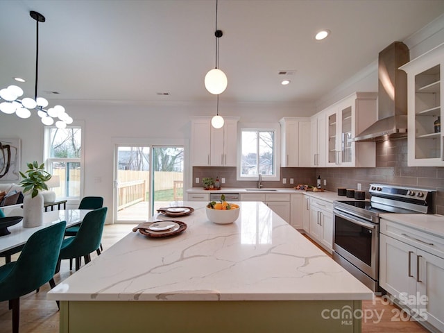 kitchen with wall chimney exhaust hood, stainless steel appliances, hanging light fixtures, and a kitchen island