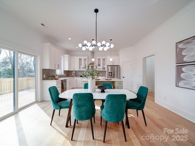 dining space featuring crown molding, a notable chandelier, sink, and light wood-type flooring