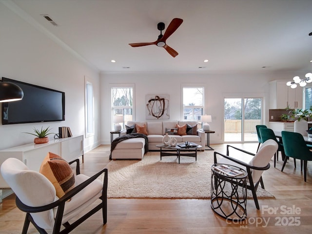 living room featuring crown molding, a wealth of natural light, ceiling fan with notable chandelier, and light wood-type flooring