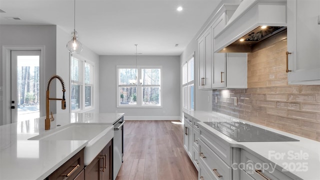 kitchen featuring black electric cooktop, white cabinets, custom exhaust hood, decorative backsplash, and pendant lighting