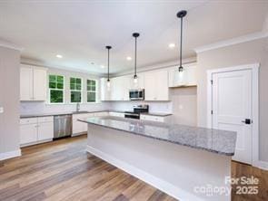 114 Glencoe Ln Unit 106, Mooresville, NC 28117 - kitchen with appliances with stainless steel finishes, white cabinets, ornamental molding, wood finished floors, and hanging light fixtures